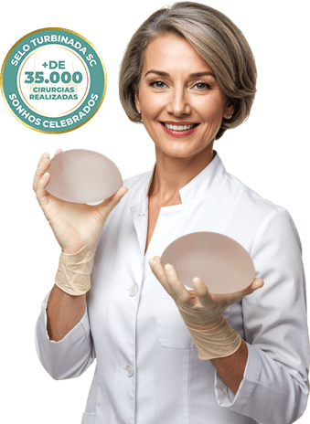 Imagem de uma mulher branca de cabelos escuros siliconada apontando para os seios com um sutiã rosa claro