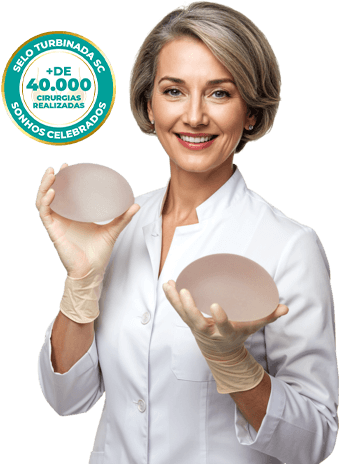 Imagem de uma mulher branca de cabelos escuros siliconada apontando para os seios com um sutiã rosa claro